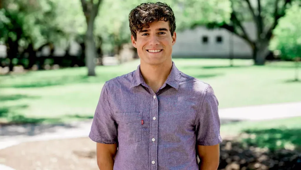 Man smiling in park wearing purple shirt.